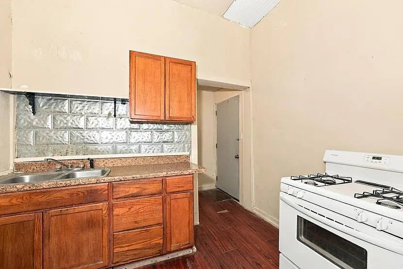 Compact kitchen with wood cabinetry, double-basin sink, tiled backsplash, and a full-size gas range for daily cooking.
