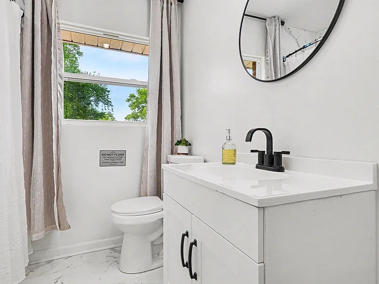 Clean full bath with a white vanity, matte-black fixtures, and a window for natural light plus a shower/tub combo.