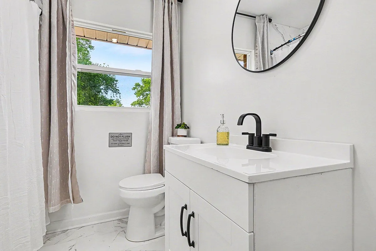 Clean full bath with a white vanity, matte-black fixtures, and a window for natural light plus a shower/tub combo. - Farmview Dr