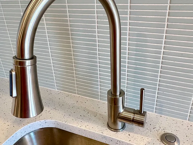 Kitchen detail showing goose neck faucet with built-in sprayer, garbage disposal button, and beautiful high-end tile backsplash.
