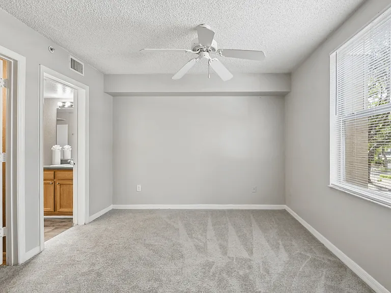 Carpeted primary bedroom with ceiling fan, large window, and en-suite bathroom access in a 3-bedroom, 2-bath apartment at Gregory Cove in Jacksonville, FL.