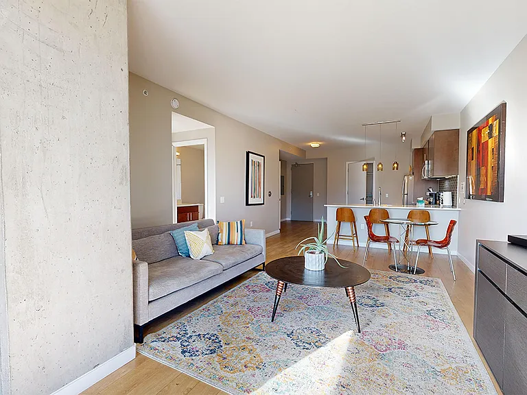 Apartment kitchen with stainless steel appliances, dining and living room with wood-style flooring.