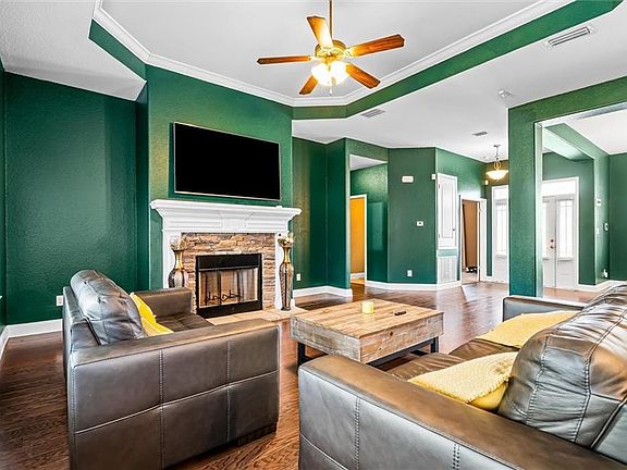 Living room featuring a fireplace, crown molding, ceiling fan, and dark wood-type flooring