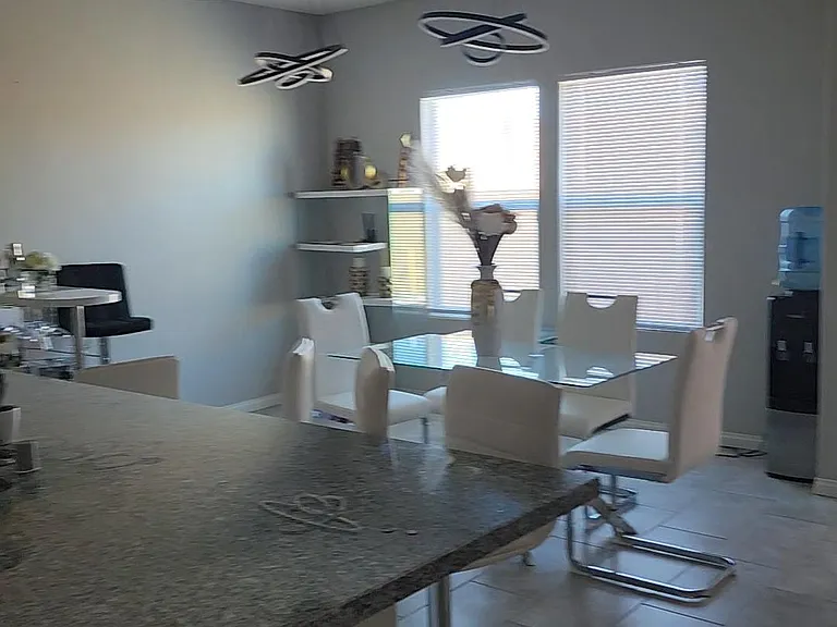 Open dining area with a glass-top table, bar seating, and large windows with blinds for natural light.