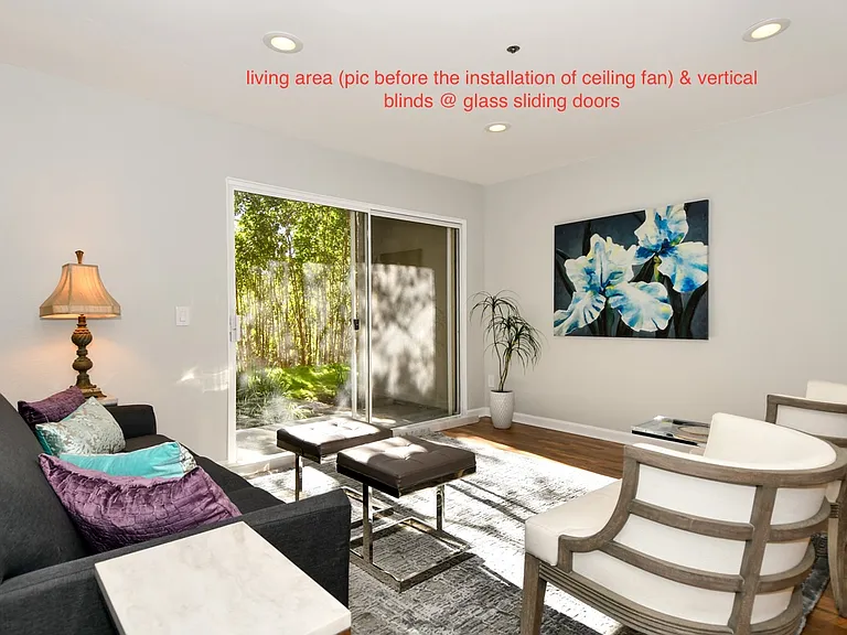 Living room area with view of private walk-out patio. Ceiling fan and vertical blinds have been installed.