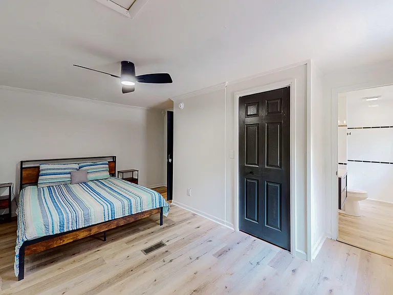 Furnished bedroom with wood-look flooring, ceiling fan, and adjacent bathroom access for added convenience.