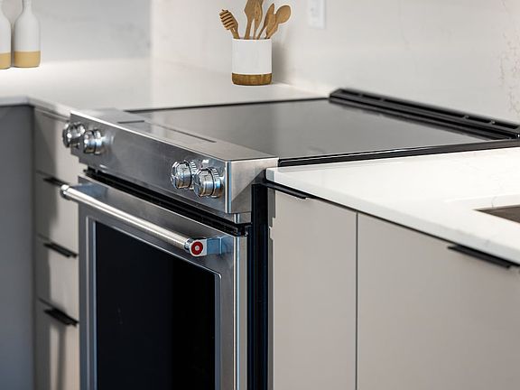 Signature Collection kitchen with light grey cabinetry, electric stove, and marbled quartz countertops and backsplash