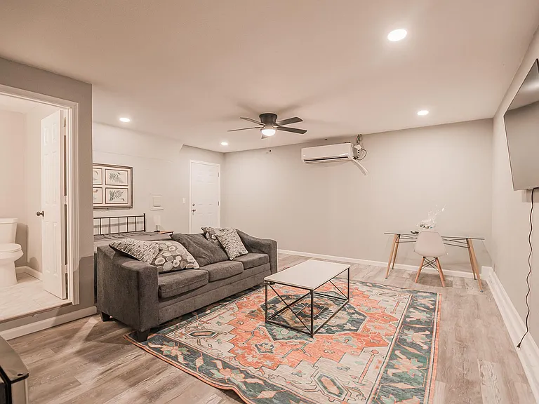Open living area with recessed lighting, ceiling fan, wall-mounted TV, and space for a small dining/work table.