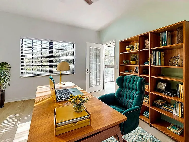 Bright home office with sleek wooden desk, teal chair, and elegant shelves filled with books, exuding warmth and style.