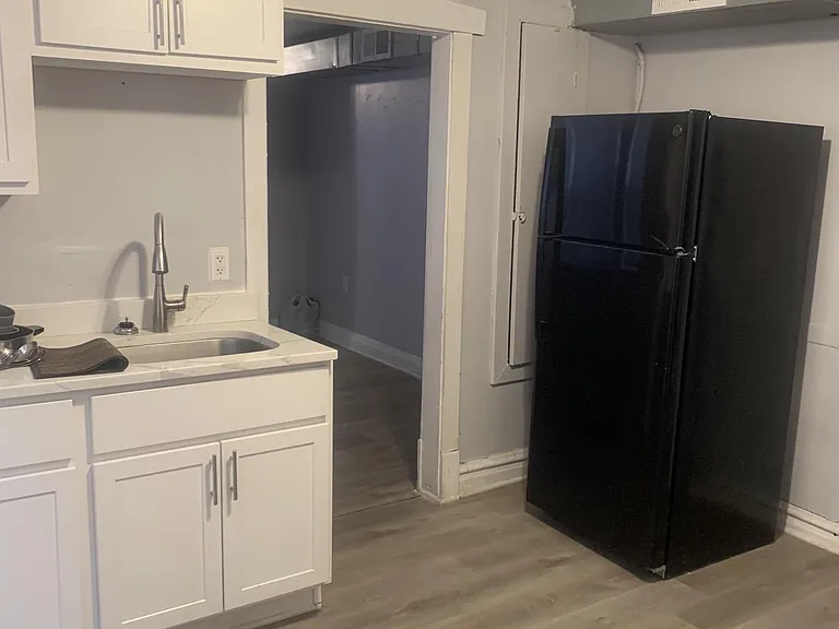 Kitchen area with shaker-style cabinetry, sink with gooseneck faucet, and a full-size refrigerator on durable flooring.