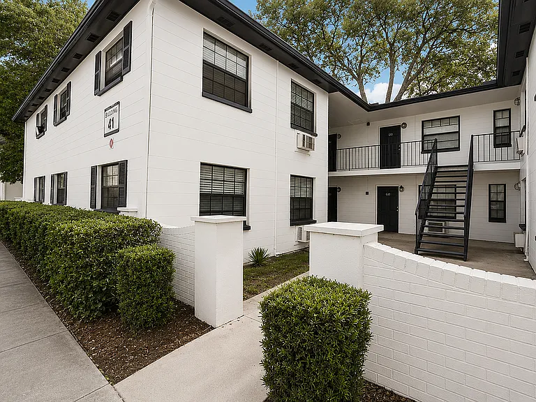 Charming multi-level white brick apartment building with lush landscaping and modern black accents, perfect for stylish urban living.