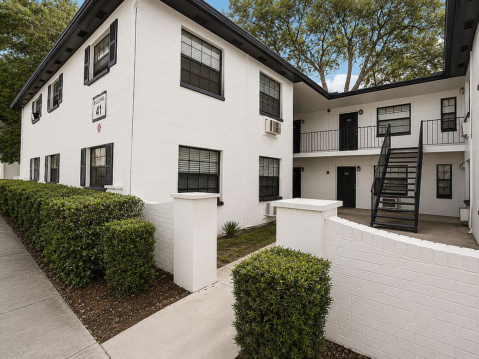 Charming multi-level white brick apartment building with lush landscaping and modern black accents, perfect for stylish urban living.
