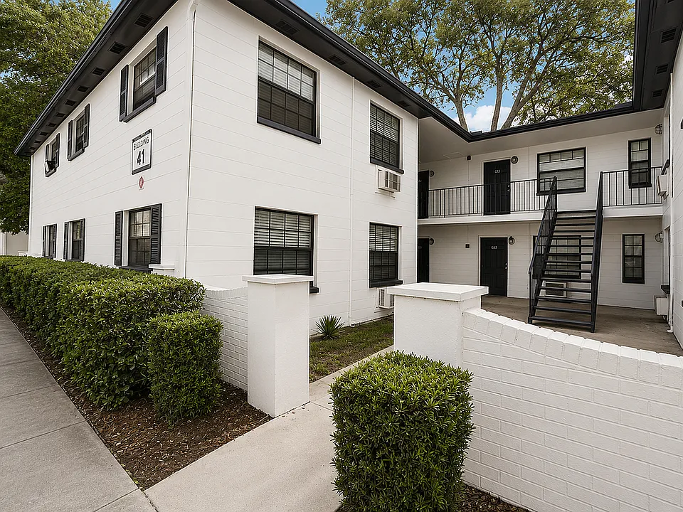 Charming multi-level white brick apartment building with lush landscaping and modern black accents, perfect for stylish urban living.
