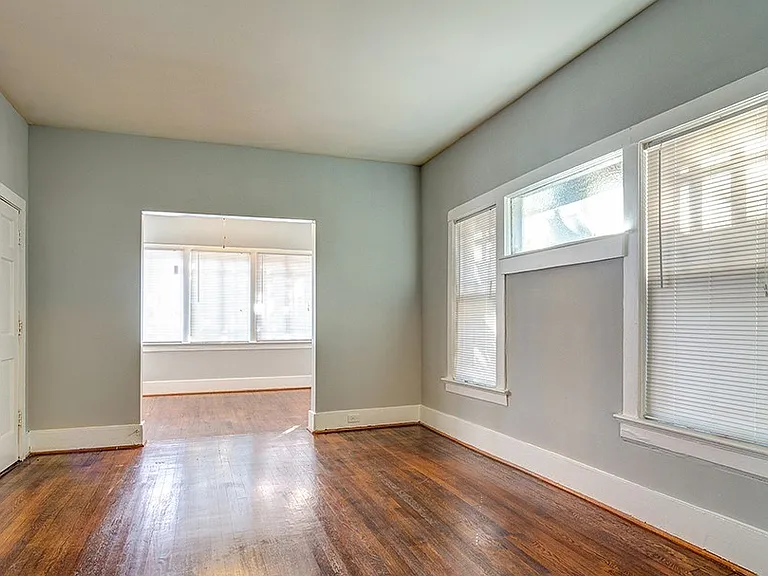 Large, open living room with hardwood floors, filled with natural light from expansive windows that create a bright, airy feel.