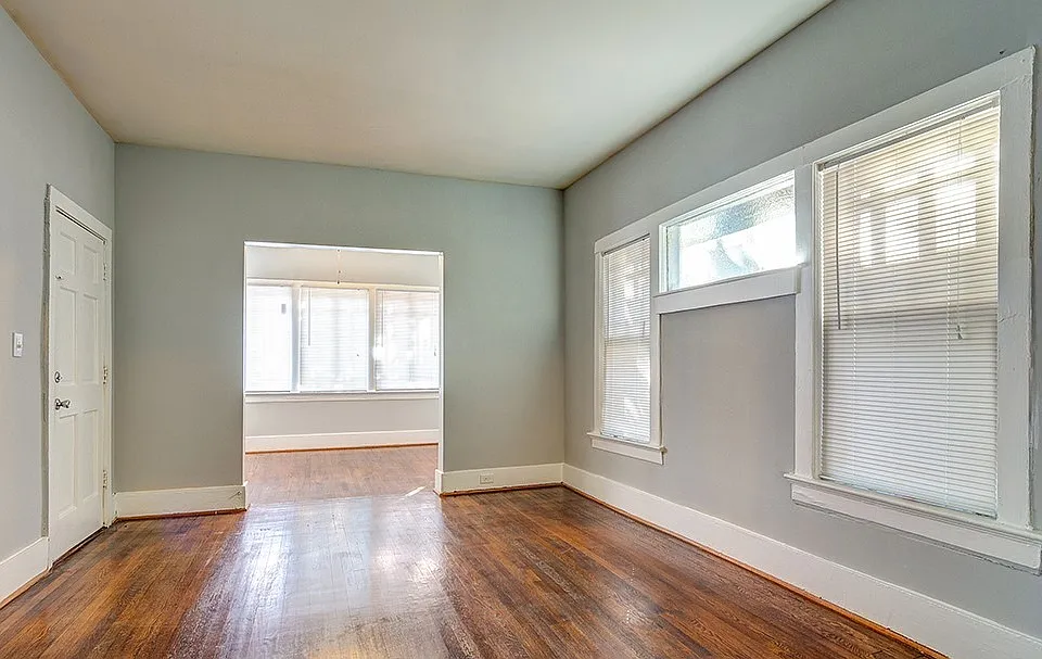 Large, open living room with hardwood floors, filled with natural light from expansive windows that create a bright, airy feel.