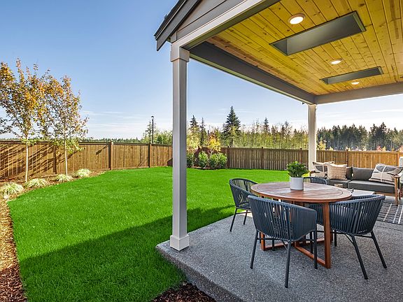 A well-manicured backyard with a covered patio, a lush green lawn, and a wooden fence surrounding th
