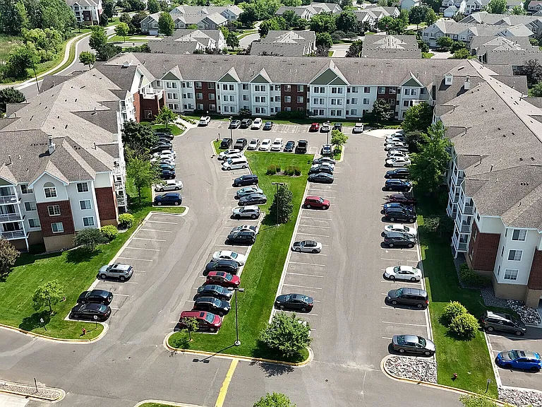 Aerial view of a modern apartment complex with spacious parking, lush greenery, and well-maintained surroundings.