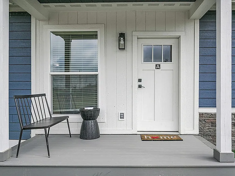 Charming front porch with a stylish bench, welcoming doormat, and pristine white door in a blue siding exterior.