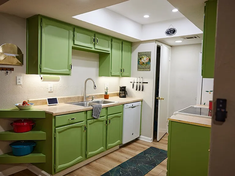 Kitchen featuring white dishwasher, open shelves, light countertops, green cabinetry, and recessed lighting
