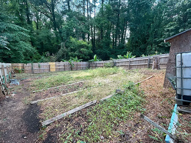 Here's the second half of the backyard. Wooden fencing continues all the way around. You'll find several rows of raised planting beds. The exterior is brimming with lush greenery and banana trees peeking through.