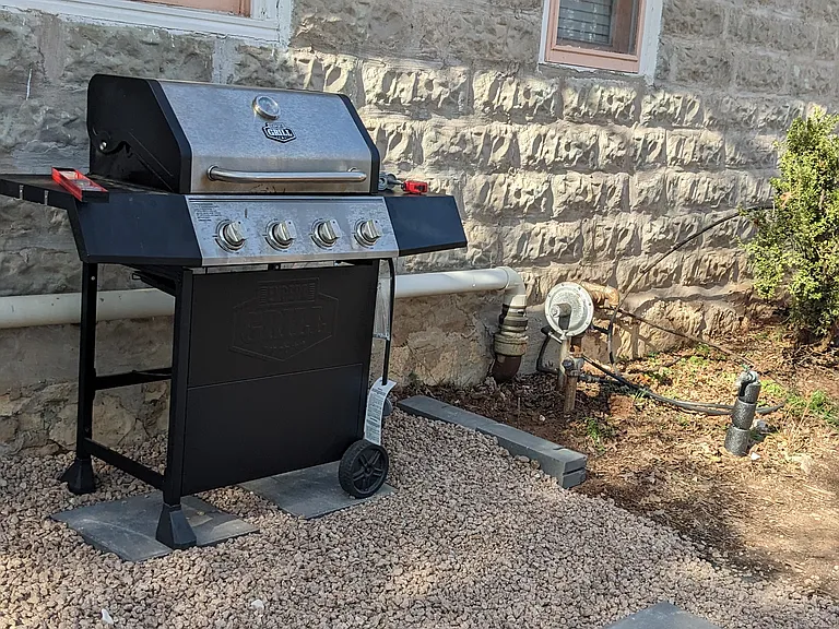 Gas grill under the kitchen window near the arbor.