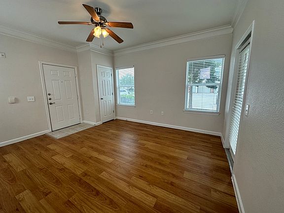 Bright living area with elegant wood-style flooring and modern ceiling fan, featuring large windows for abundant natural light. Bright living area with elegant wood-style flooring and modern ceiling fan, featuring large windows for abundant natural light.