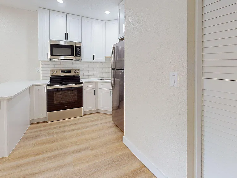 Modern kitchen with sleek stainless steel appliances, elegant white cabinetry, and warm wooden flooring, offering a stylish and functional space.