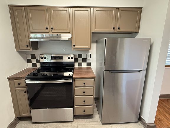 New stove and refrigerator with ceramic tile backsplash and freshly painted cabinets.