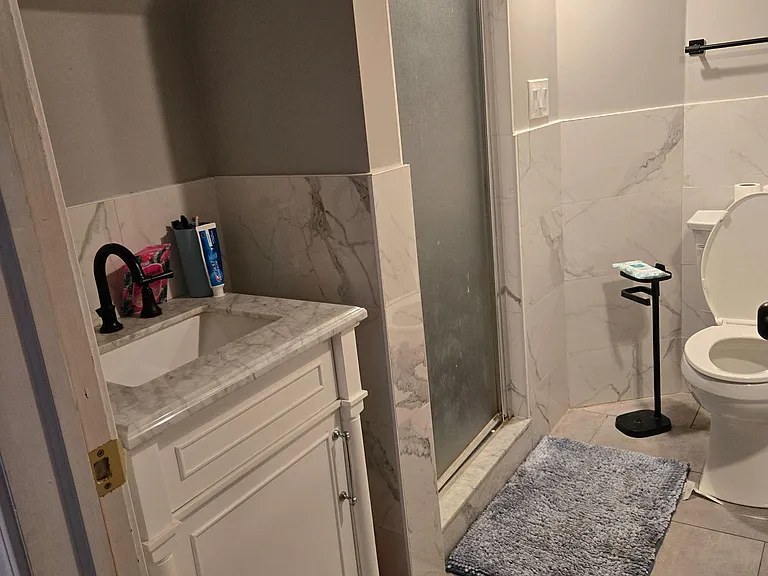 Updated bathroom with marble-look tile surround, vanity sink, and sliding glass shower for easy daily use.