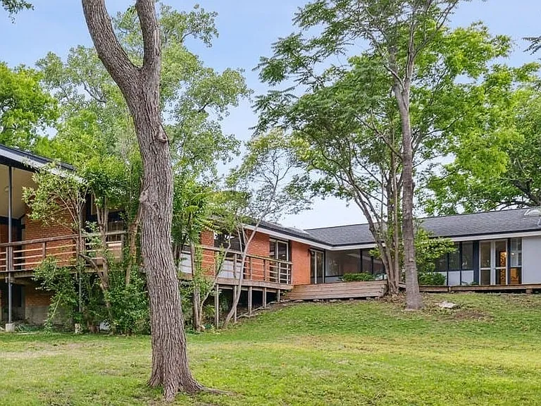 Mid-century modern residence featuring extensive decking, brick exterior, sloped roofline, and abundant natural light through large windows