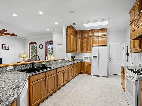 Spacious kitchen featuring extensive wood cabinetry, light-toned granite countertops, a black double basin sink with a gooseneck faucet, a white gas range, and recessed lighting