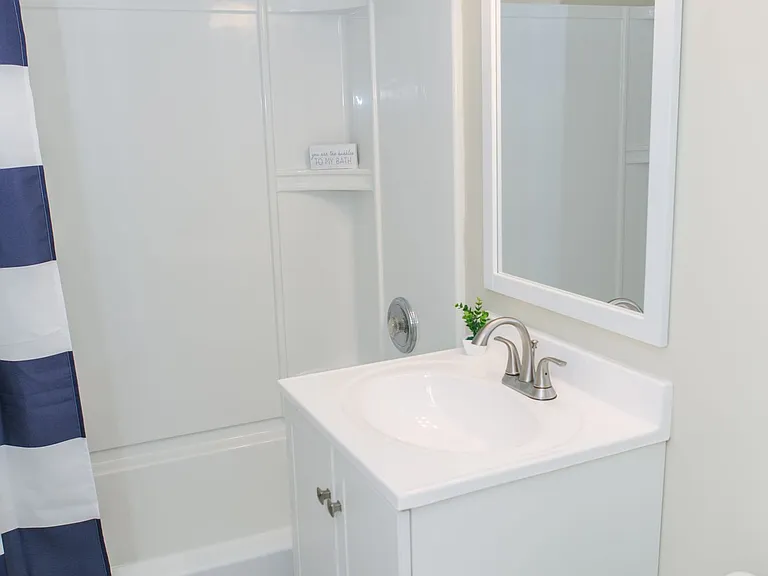 Crisp White Full Bath With Shower, White Sink And Cabinets With Updated Lights And Mirror.
