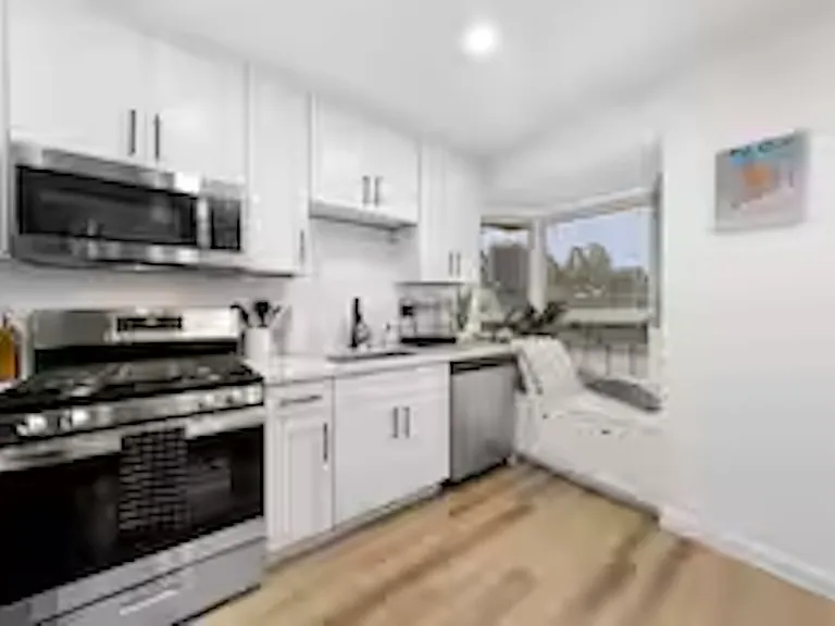 Modern kitchen with white cabinetry, stainless steel appliances, and stone benchtops, featuring a coffee machine, blender, stove cooktop, and plenty of natural light.