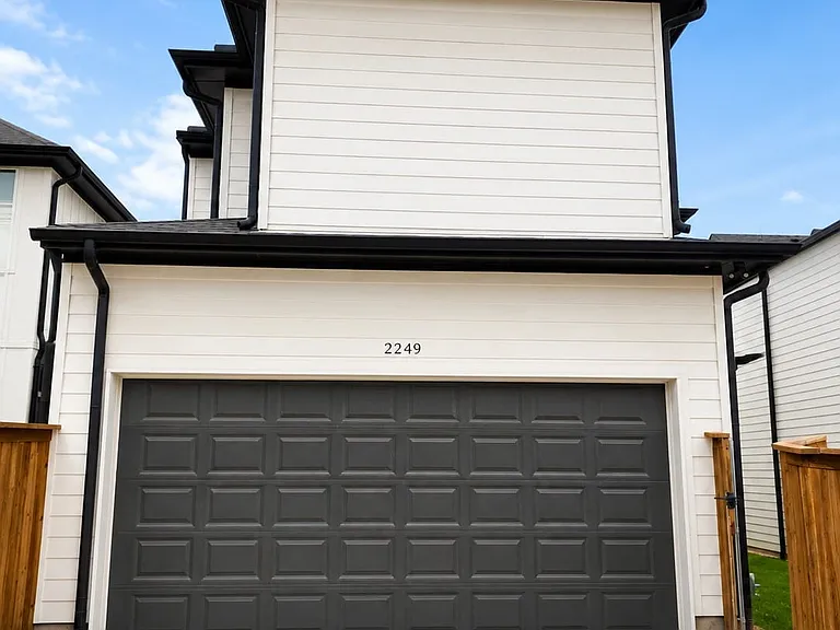 Front exterior featuring white horizontal siding, black trim, and a dark grey paneled garage door