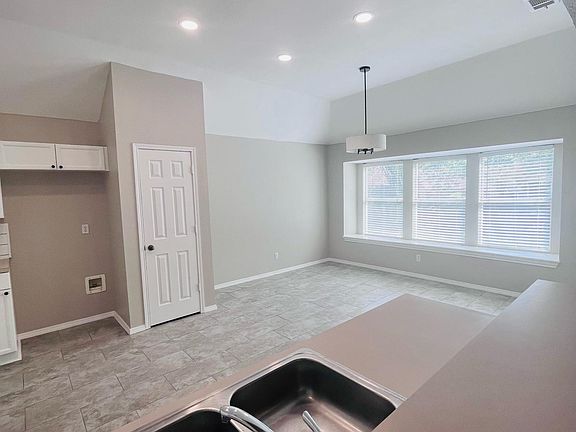 Well lit kitchen with lights and large windows. View from living room.