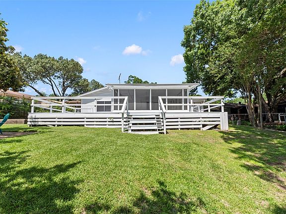Spacious rear yard with a sloped lawn, a large wood deck with railings, and a screened-in porch