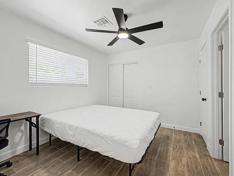 Bedroom with a ceiling fan, window with blinds, and double-door closet, plus space for a bed and work desk.