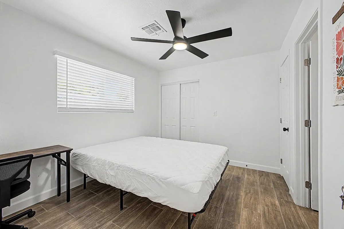 Bedroom with a ceiling fan, window with blinds, and double-door closet, plus space for a bed and work desk. - W 6th Dr