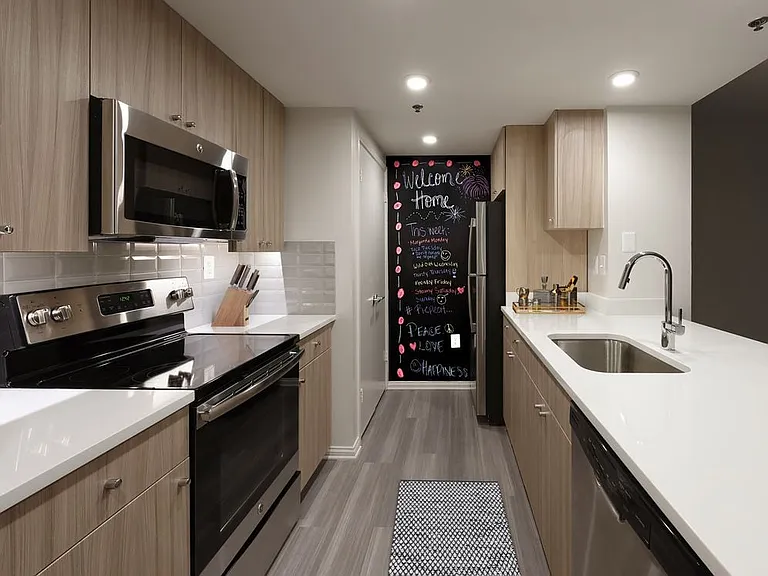 Renovated Package II kitchen with white quartz countertops, white tile backsplash, driftwood cabinetry, stainless steel appliances, and hard surface plank flooring
