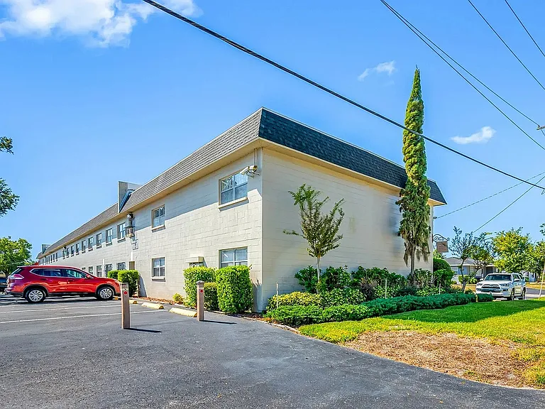 Charming apartment building with lush greenery and ample parking, set in a peaceful neighborhood under clear blue skies.