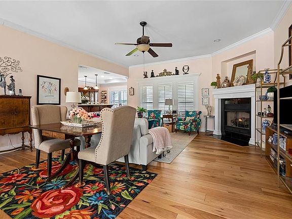 Living room with a fireplace with flush hearth, ceiling fan, light wood-style flooring, and ornamental molding