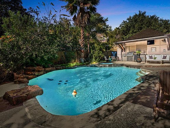 A sparkling pool and spa, rock waterfall, multiple seating areas, patio decking, covered outdoor kitchen, and stunning outdoor lighting.