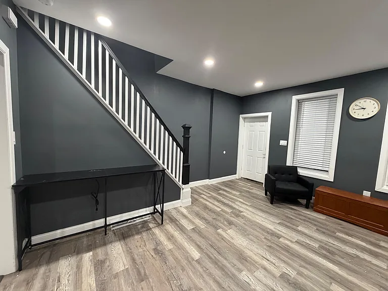 Open common area by the staircase with durable plank flooring, recessed lighting, and a window with blinds for privacy.