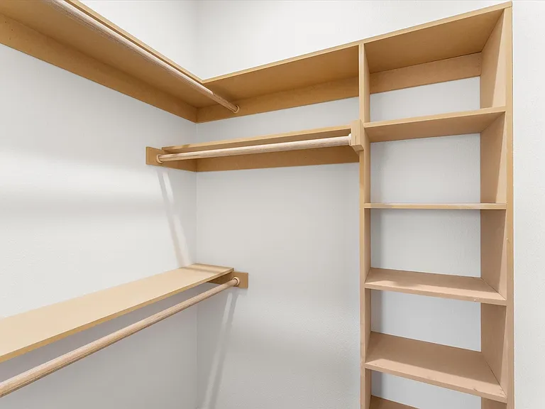 Built-in closet organization system featuring light wood-finish shelving and multiple hanging rods