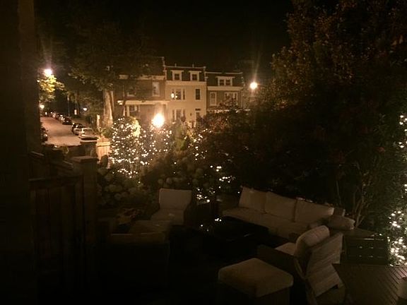 View of yard at night with lights on trees, entrance to apartment through this patio.