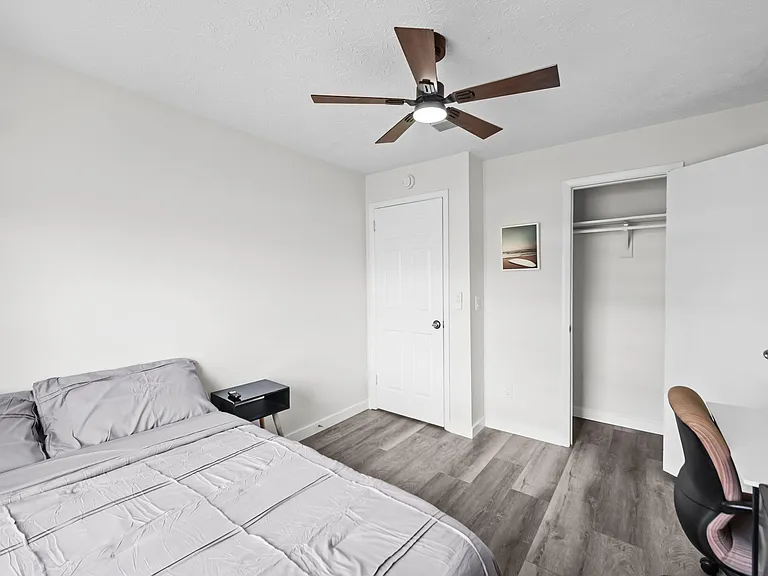 Private bedroom with ceiling fan, wood-style flooring, and an open closet; space for a bed plus a compact desk setup.