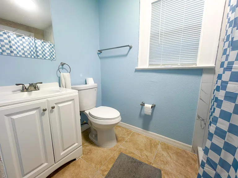 Full bath with a single-sink vanity, tiled flooring, and a window with blinds for ventilation and natural light.