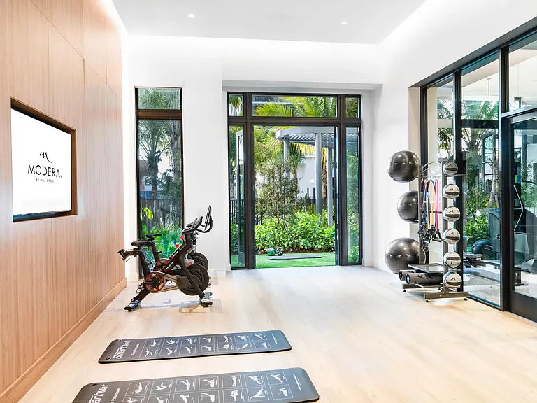A light-filled fitness studio at Modera Aventura, designed with warm wood tones and direct garden access for an indoor-outdoor workout experience.