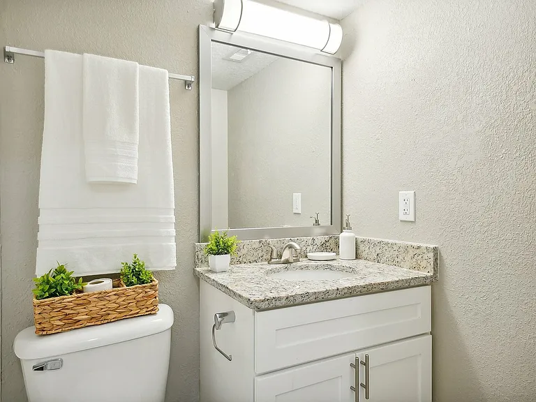 Elegant bathroom with granite countertop, large mirror, and fresh white towels, accented by a woven basket with greenery for a welcoming touch.