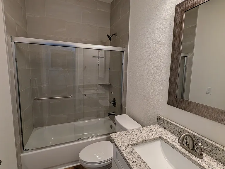 Hall bathroom with granite countertop, toilet, and bathtub with glass sliding door.